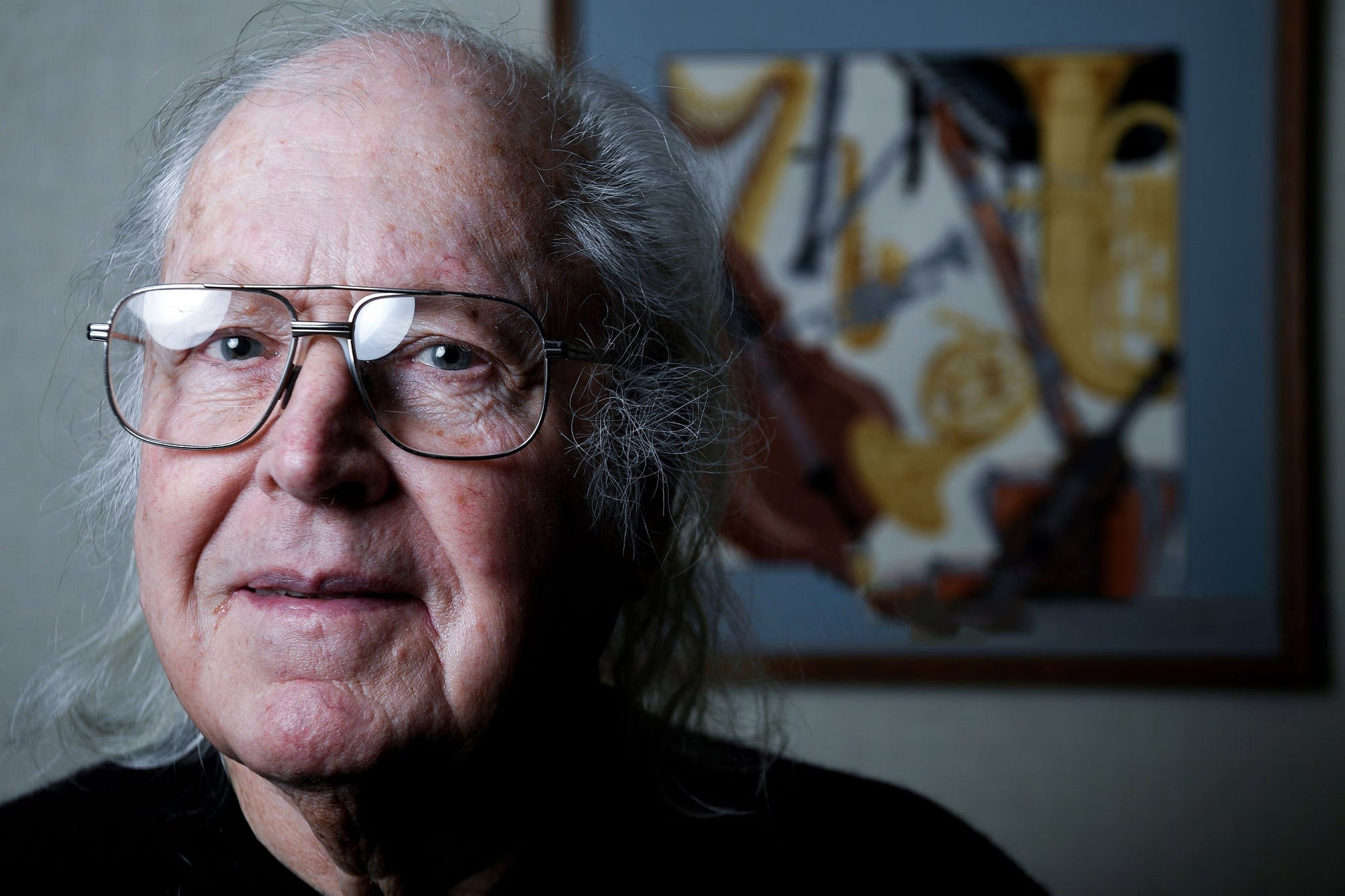 An older man with glasses in front of a painting.