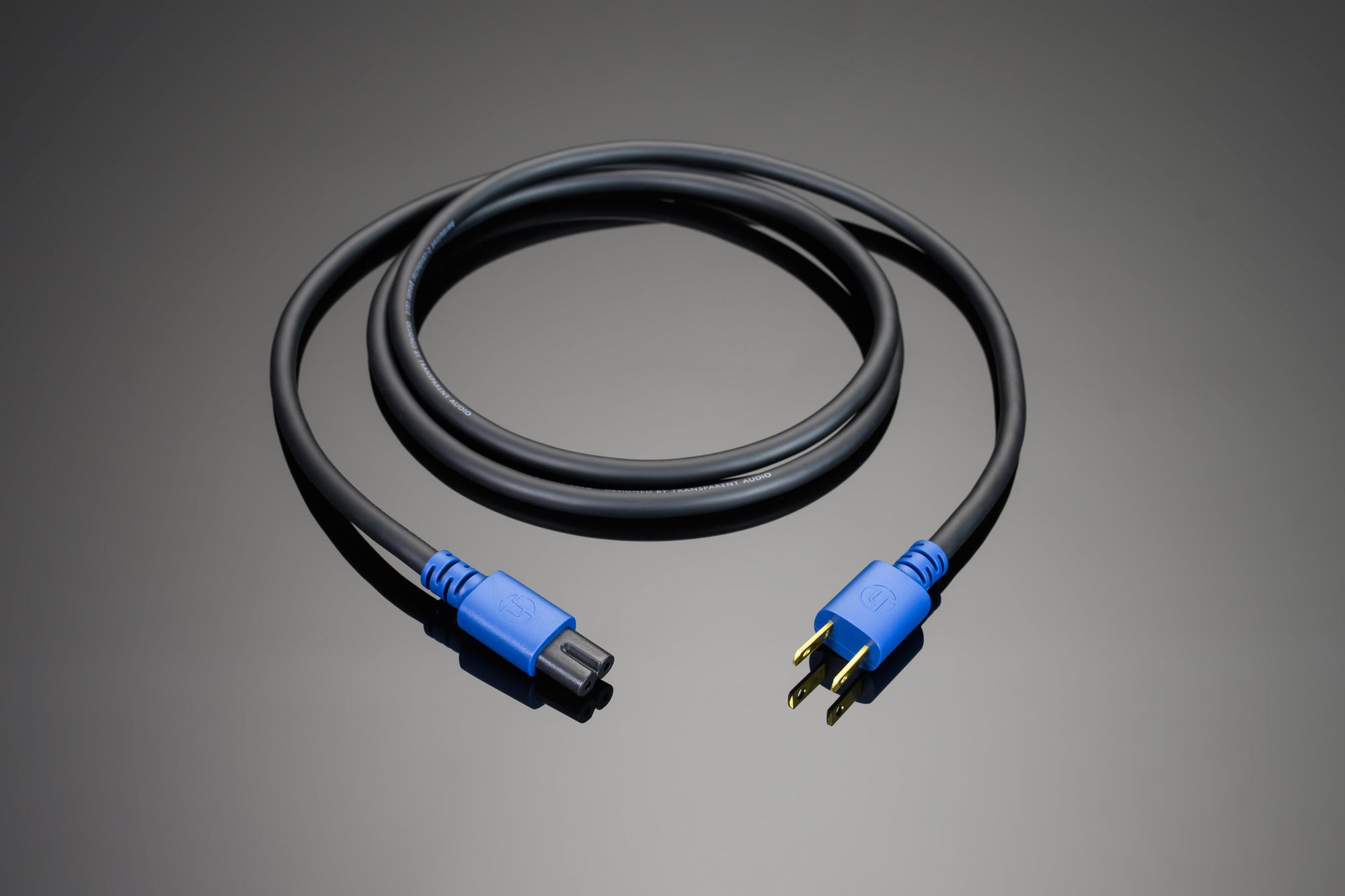 A coiled black and blue Transparent Audio Hardwired 2-Conductor Power Cord with a two-pronged plug on one end and a corresponding socket on the other, placed on a gray surface.