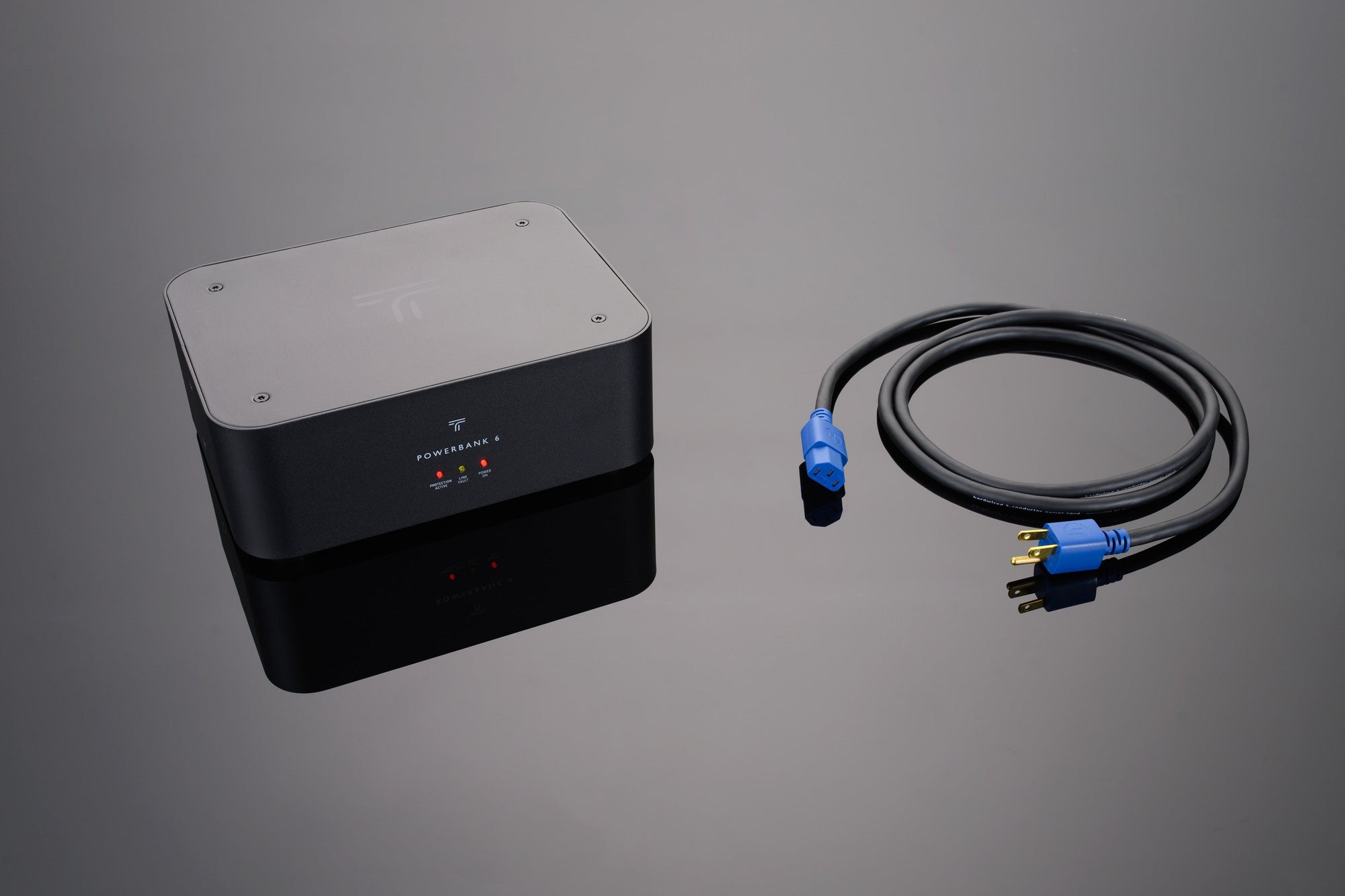 A PowerBank 6 Power Conditioner by Transparent Audio, along with a blue and yellow plug-in cable, is displayed on a reflective surface.