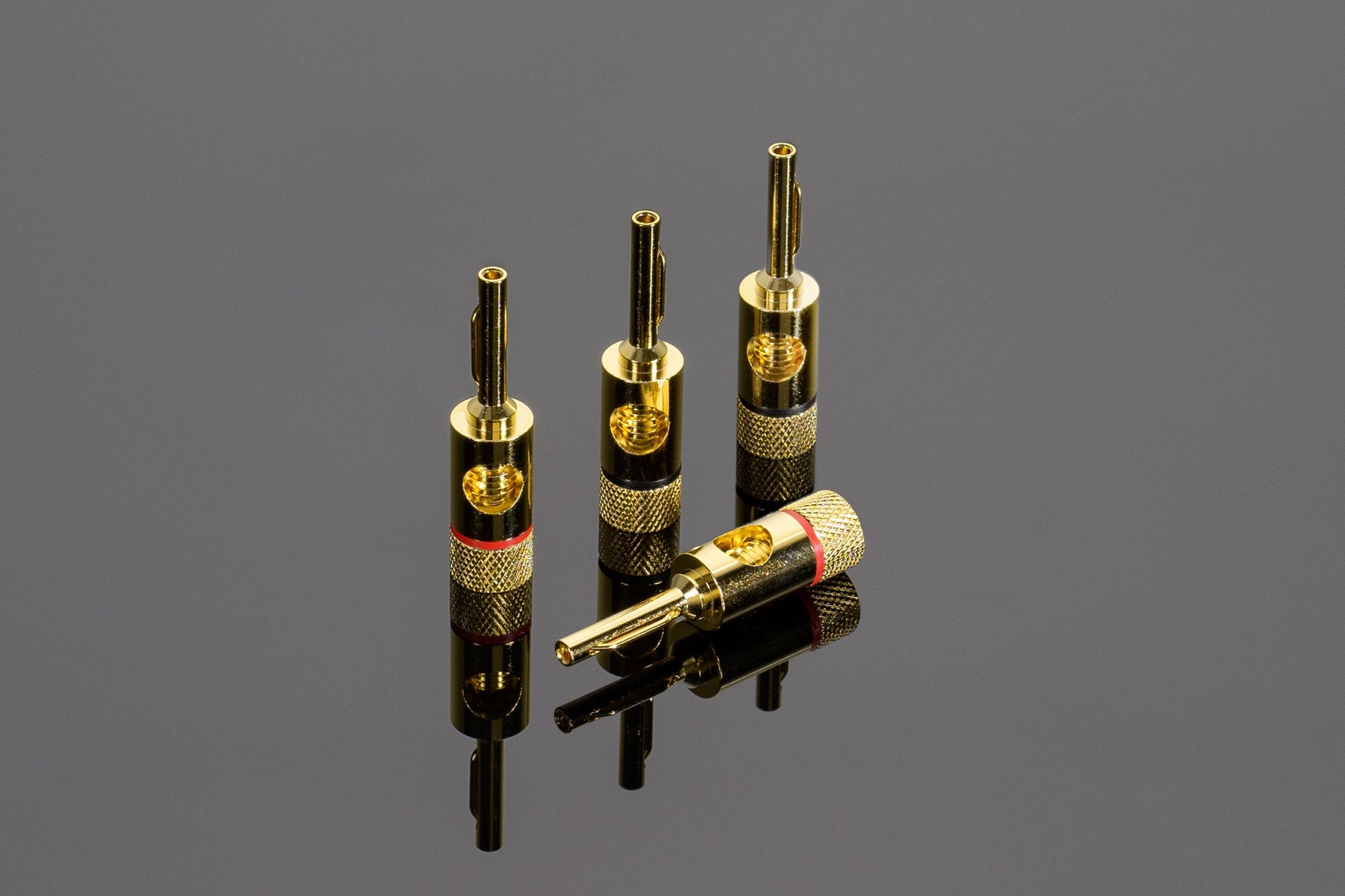 Four Transparent Spade to Banana Adapters by Transparent Audio, three standing upright and one lying down, are displayed on a reflective surface, perfect for enhancing your speaker cables.