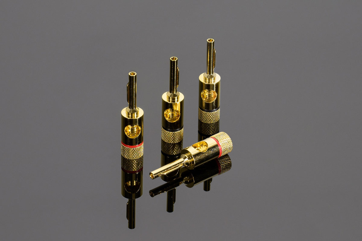 Four Transparent Spade to Banana Adapters by Transparent Audio, three standing upright and one lying down, are displayed on a reflective surface, perfect for enhancing your speaker cables.
