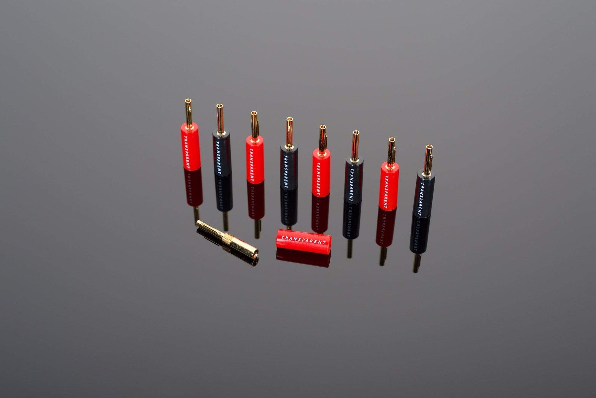 A set of nine Transparent Audio Crimp Banana Connectors, featuring five red and four black plugs, neatly arranged in a row on a reflective surface.