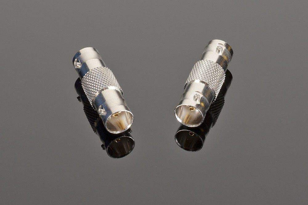 Two high-quality Female BNC to Female BNC connectors from Transparent Audio are placed on a reflective dark surface, perfect for enhancing your home entertainment setup.