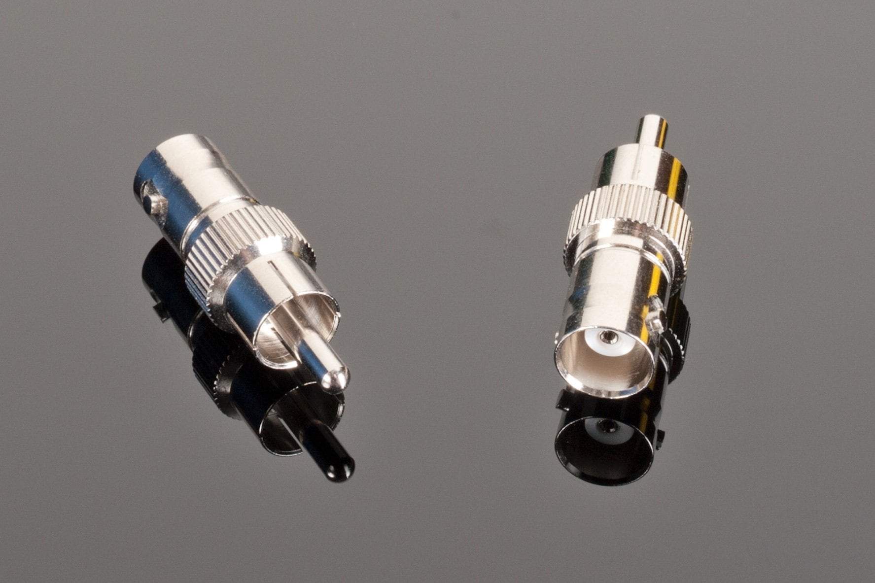 Two high-quality Transparent Audio Female BNC to Male RCA connectors on a reflective black surface, one facing up showing the pin, the other facing down revealing the socket. Perfect for home entertainment systems or as digital audio adapters.