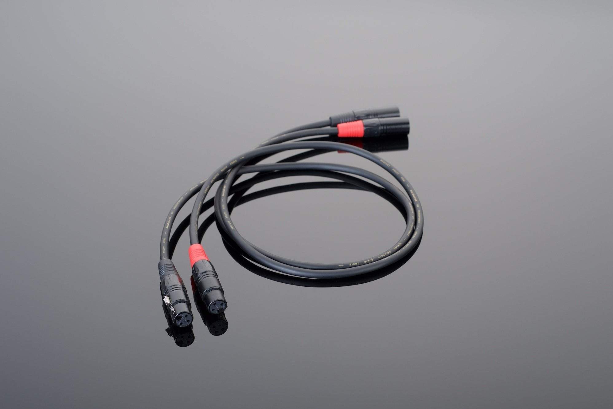 The Hardwired Balanced Interconnect by Transparent Audio features a black coaxial cable with red connectors, elegantly blending into your system companions on a reflective gray surface.