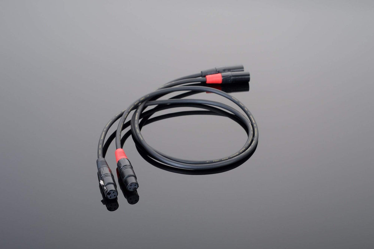 The Hardwired Balanced Interconnect by Transparent Audio features a black coaxial cable with red connectors, elegantly blending into your system companions on a reflective gray surface.