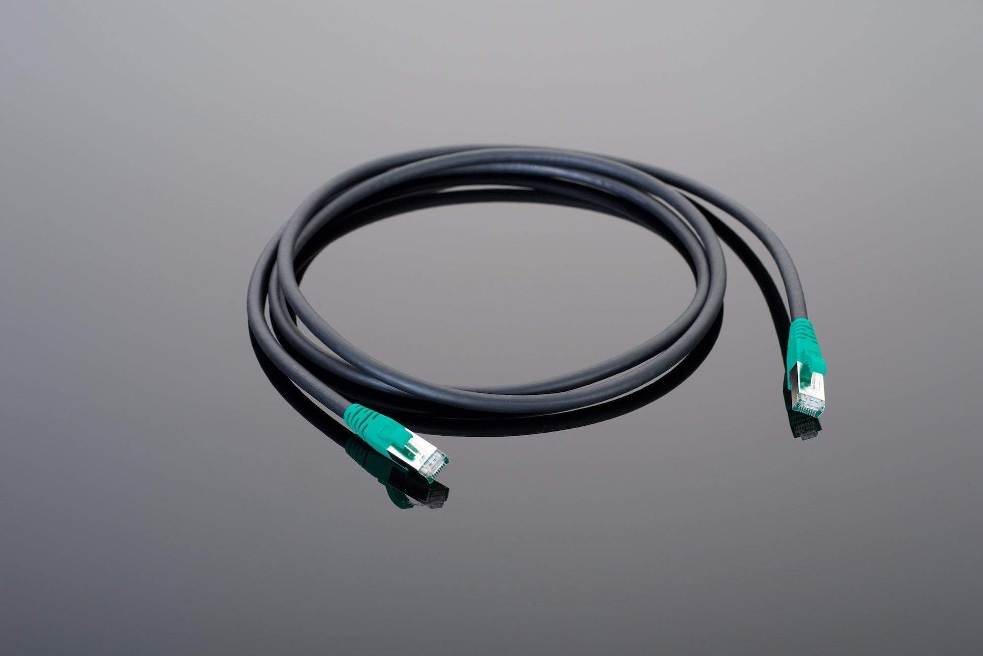 A coiled Transparent Audio Hardwired Ethernet cable with black coating and green connectors at both ends, perfect for hardwired Ethernet connections, laid on a reflective surface.