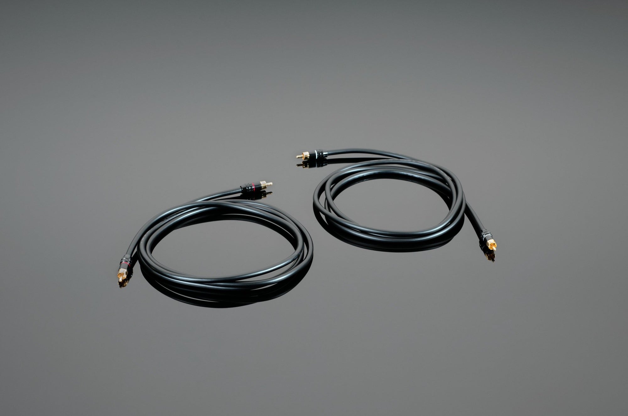 Two coiled Hardwired RCA Interconnect cables in black with gold-plated connectors from Transparent Audio, perfect for basic music and film systems, placed on a smooth, gray surface.