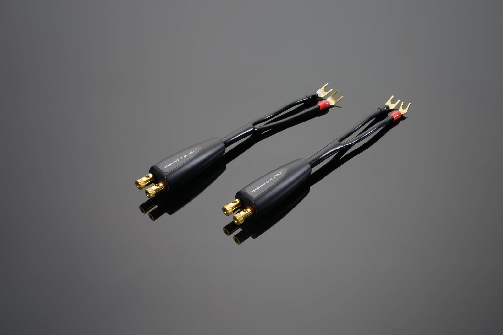 Two High Performance 10-2 Brick and 10-2 Brick Biwire Networks speaker cables from Transparent Audio, featuring gold-plated connectors, are displayed side by side on a grey background, ready to deliver exceptional low-frequency energy.