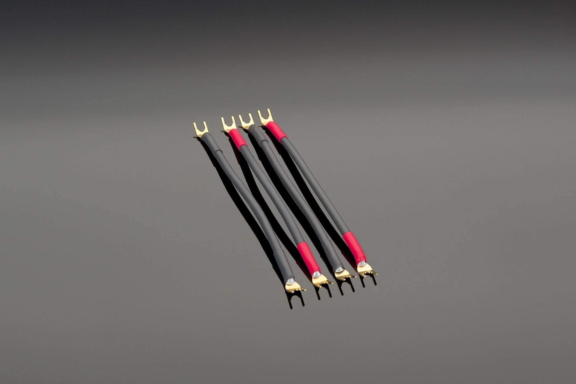 Four Transparent Audio High Performance Biwire Speaker Adapters, featuring black and red cables with gold-plated connectors and high-purity copper strands, are arranged in parallel on a grey surface.