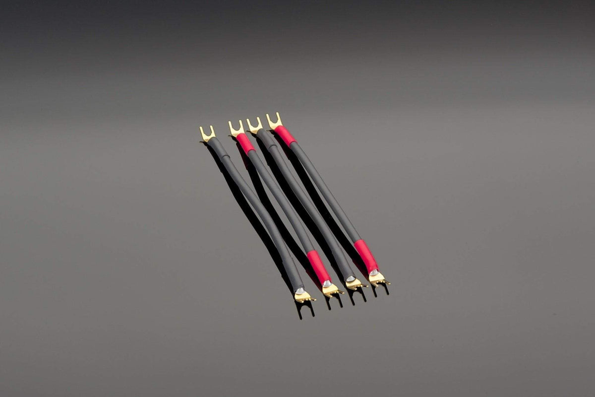 Four Transparent Audio High Performance Biwire Speaker Adapters, featuring black and red cables with gold-plated connectors and high-purity copper strands, are arranged in parallel on a grey surface.