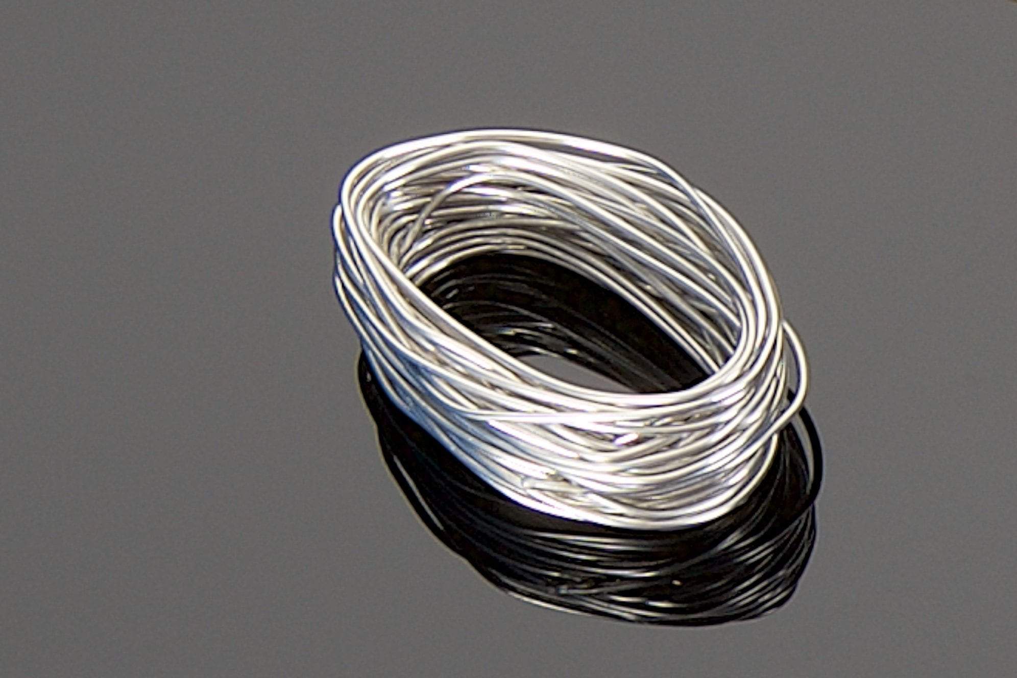 A coiled bundle of the Transparent Audio High Silver Content, Lead-Free Solder Pack rests on a reflective black surface, boasting a 15-foot length of thin silver wire.