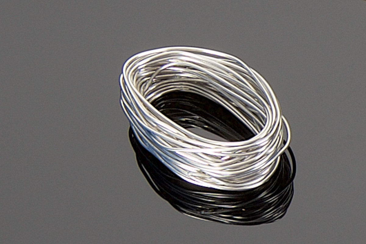 A coiled bundle of the Transparent Audio High Silver Content, Lead-Free Solder Pack rests on a reflective black surface, boasting a 15-foot length of thin silver wire.