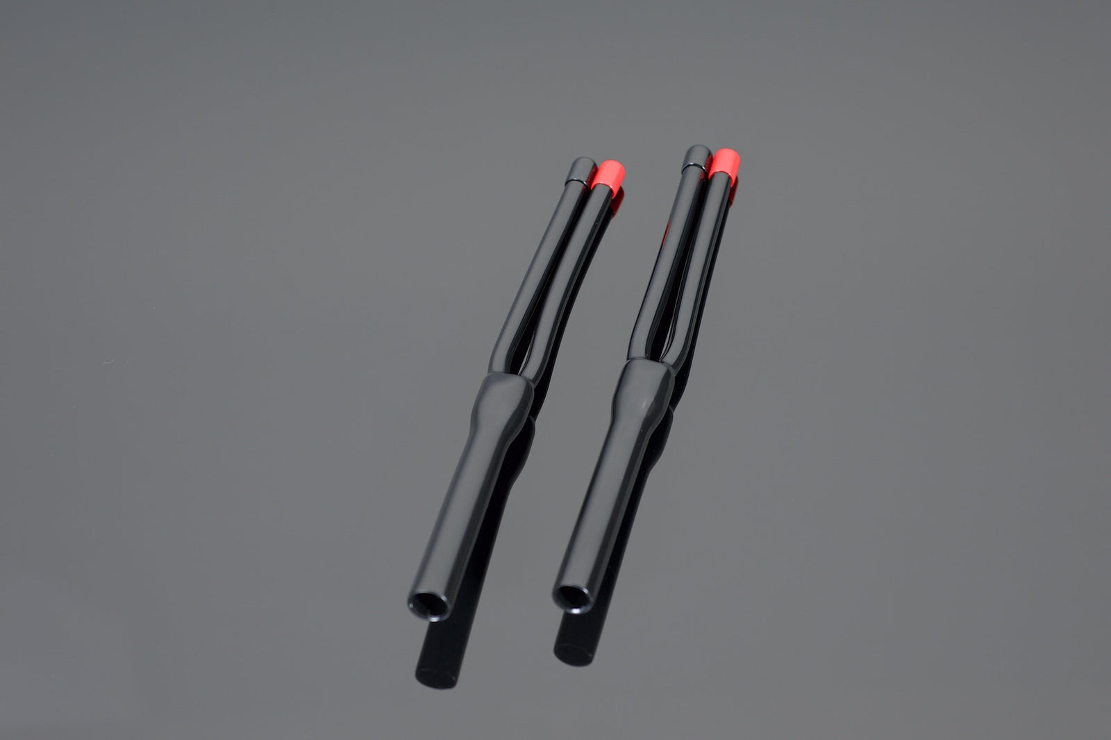 Placed parallel to each other on a gray background, two black Transparent Audio HP10-2 Speaker Cable Termination Boots with red tips exude a professional appearance.