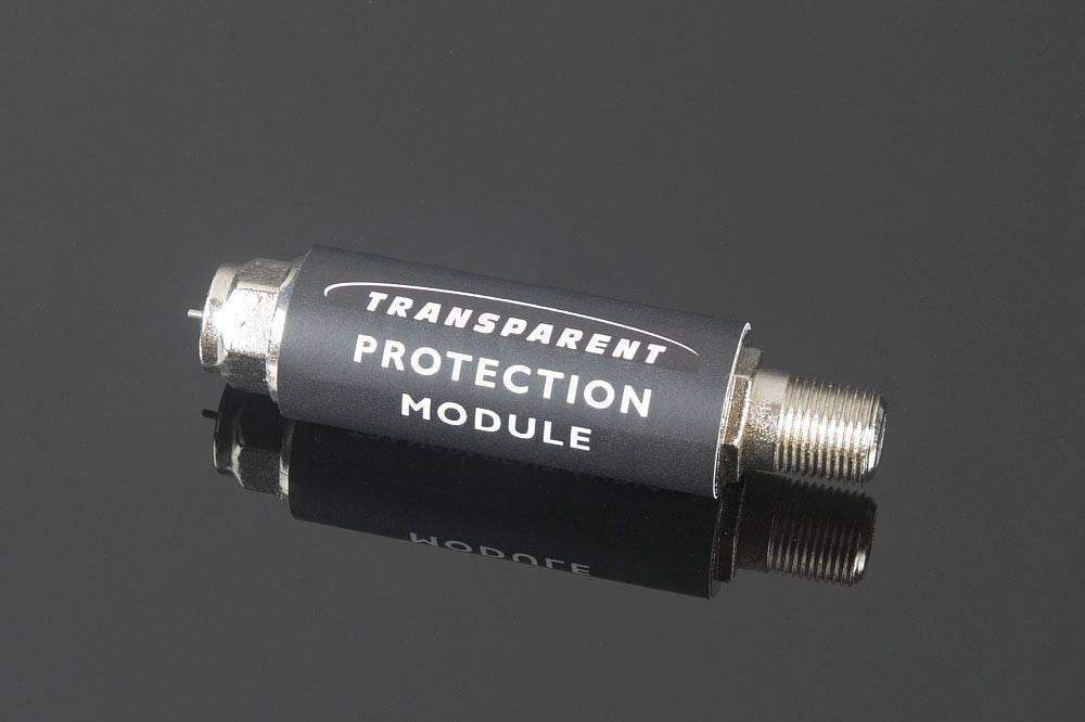 A small black cylindrical device, branded "In-Line Coaxial Protector" by Transparent Audio and designed for surge protection in CATV systems, with metal connectors on both ends, lies on a reflective black surface.