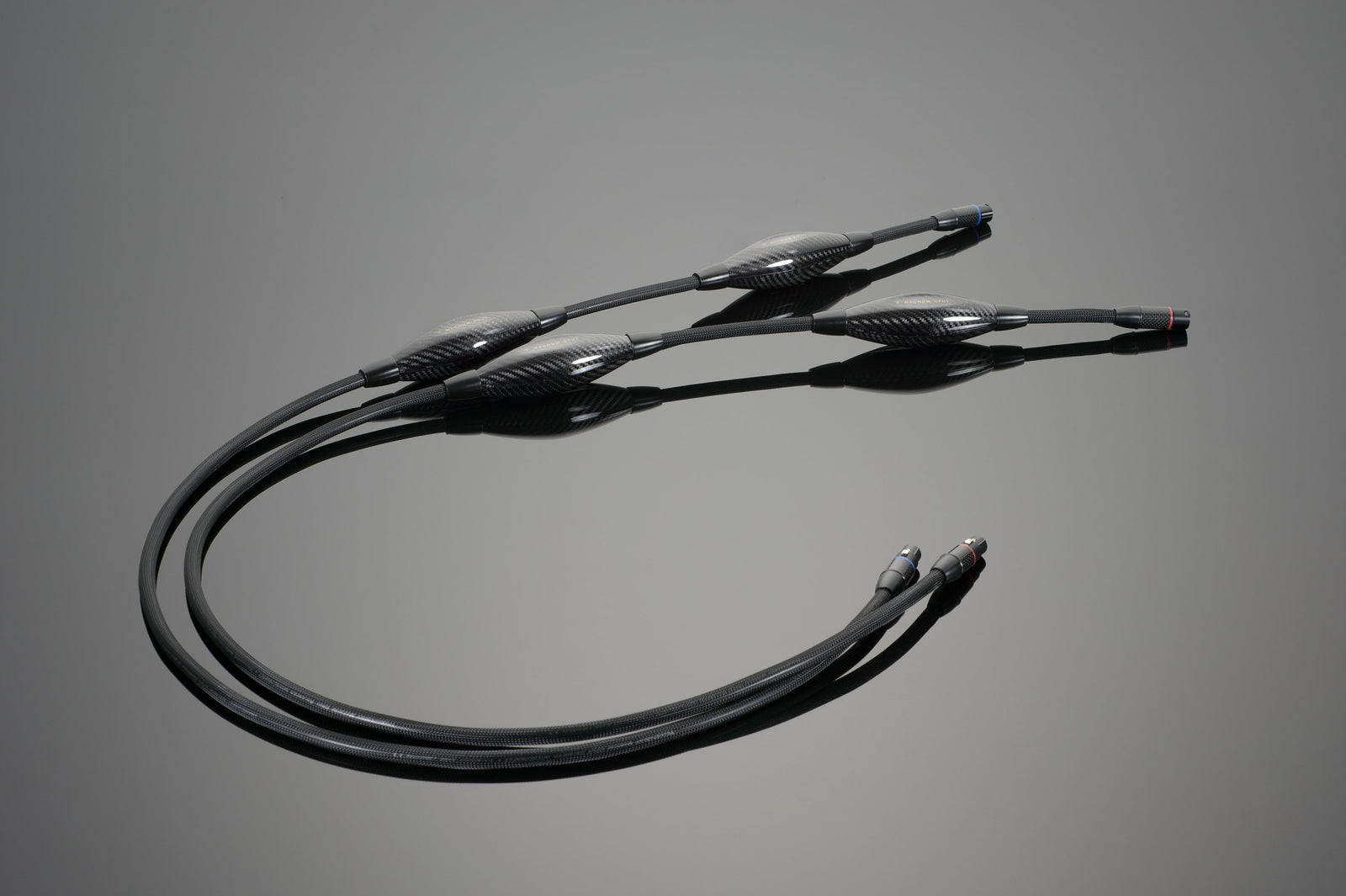 A set of MAGNUM OPUS Balanced Interconnect cables from Transparent Audio with intricate connectors lies on a smooth, grey surface.