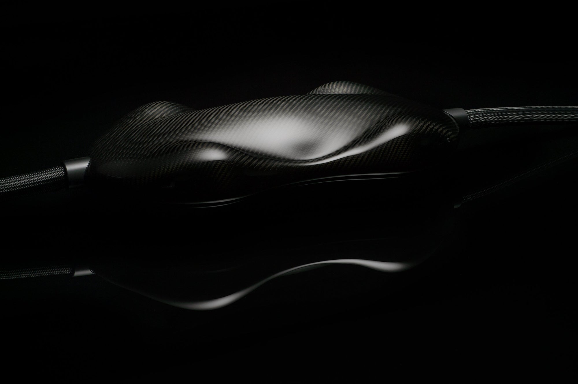 A glossy, black carbon fiber object with a smooth, contoured surface connected to Transparent Audio MAGNUM OPUS Speaker Cable is set against a dark background.