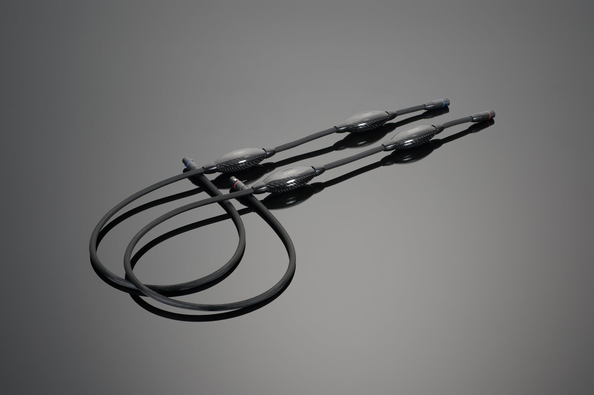 Three black Transparent Audio OPUS Balanced Interconnects, each featuring cylindrical connectors on both ends, are coiled on a neutral background.