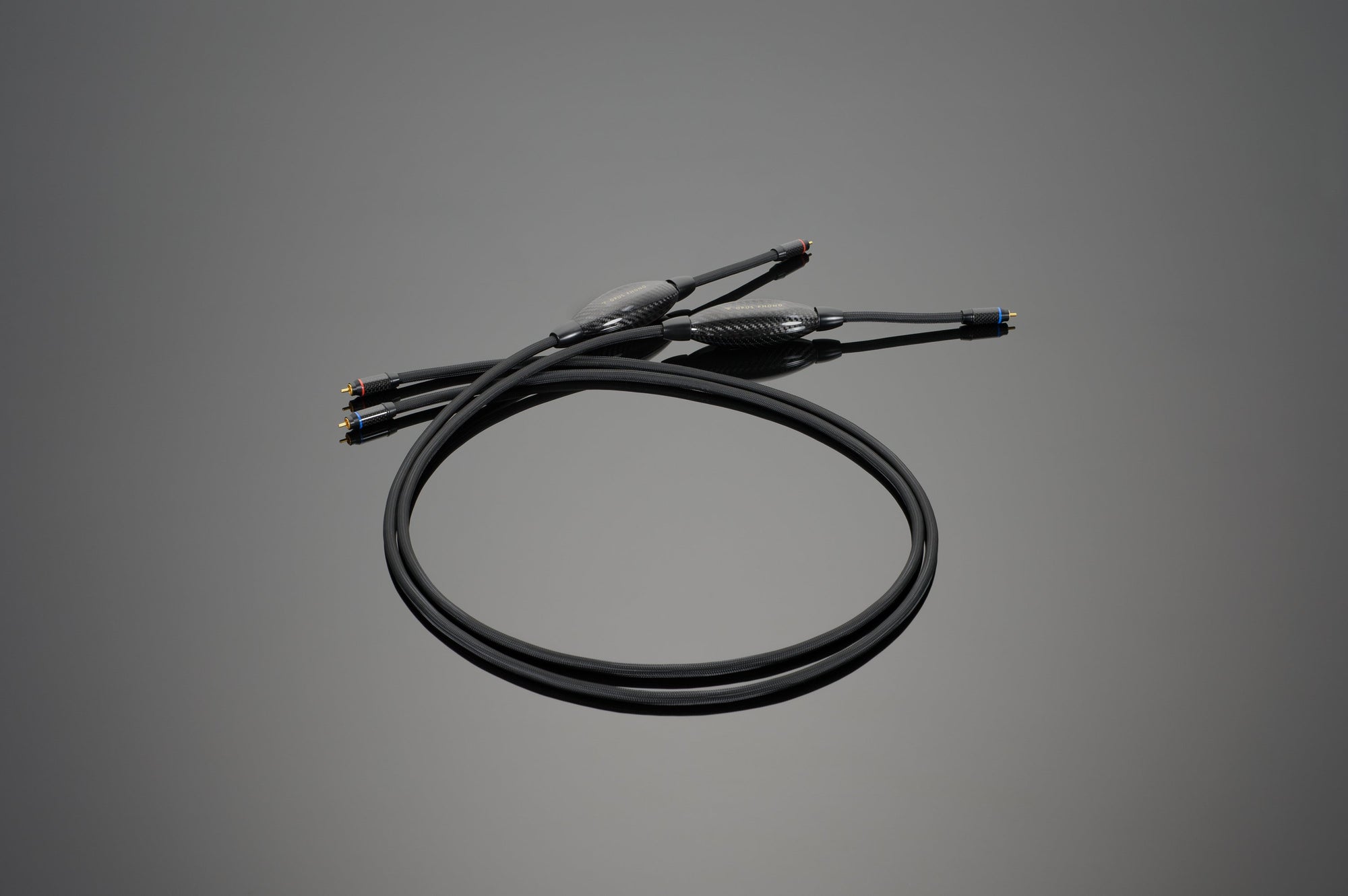 The OPUS Phono Interconnect by Transparent Audio, a black coaxial cable with connectors on both ends, is coiled on a gray background, making it ideal for an ultimate LP playback system.