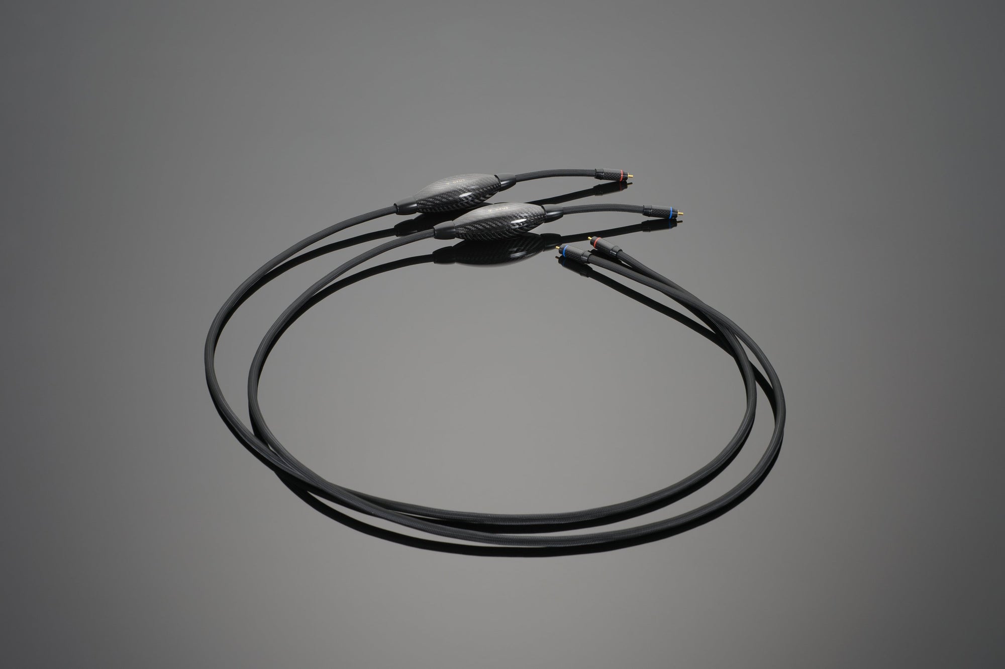 A pair of black audio cables with connectors on both ends, lying on a gray surface, these Transparent Audio OPUS RCA Interconnects boast Upgraded Connoisseur Level quality for exceptional audio performance.