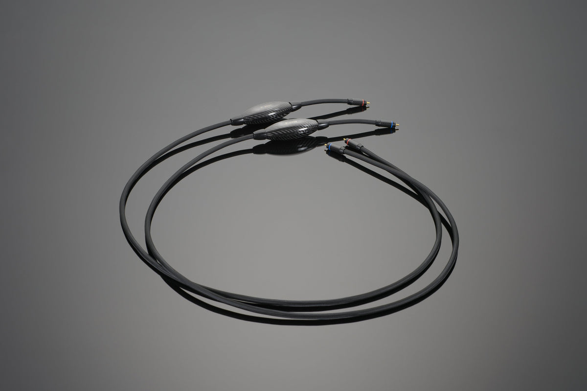 A pair of black audio cables with connectors on both ends, lying on a gray surface, these Transparent Audio OPUS RCA Interconnects boast Upgraded Connoisseur Level quality for exceptional audio performance.