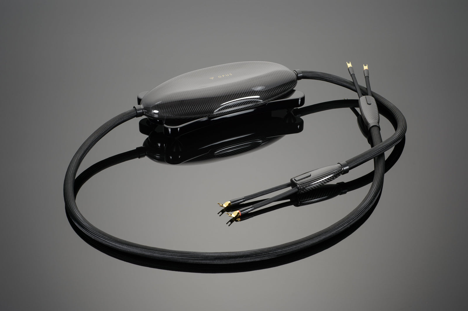 A high-quality Transparent Audio OPUS Speaker Cable featuring gold-plated connectors, a carbon fiber housing, and a sleek black braided outer sheath, elegantly displayed on a reflective surface.