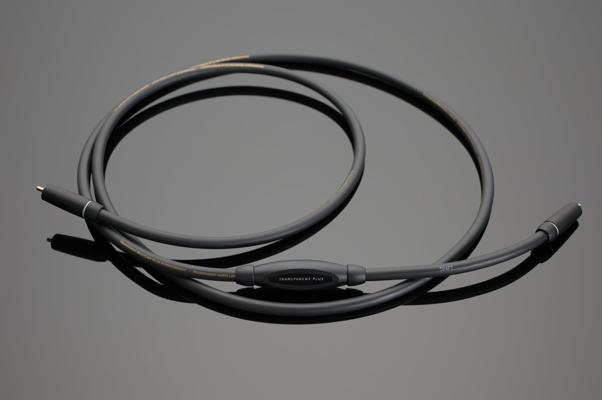 A black coaxial cable with gold-plated connectors on both ends is coiled on a grey surface, showcasing refined dynamics and performance akin to the Transparent Audio PLUS RCA Interconnect.
