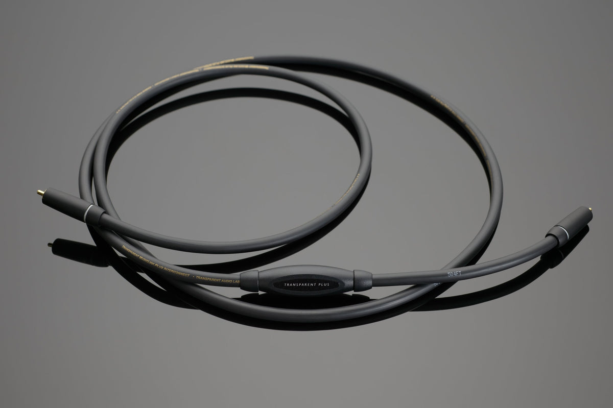 A black coaxial cable with gold-plated connectors on both ends is coiled on a grey surface, showcasing refined dynamics and performance akin to the Transparent Audio PLUS RCA Interconnect.