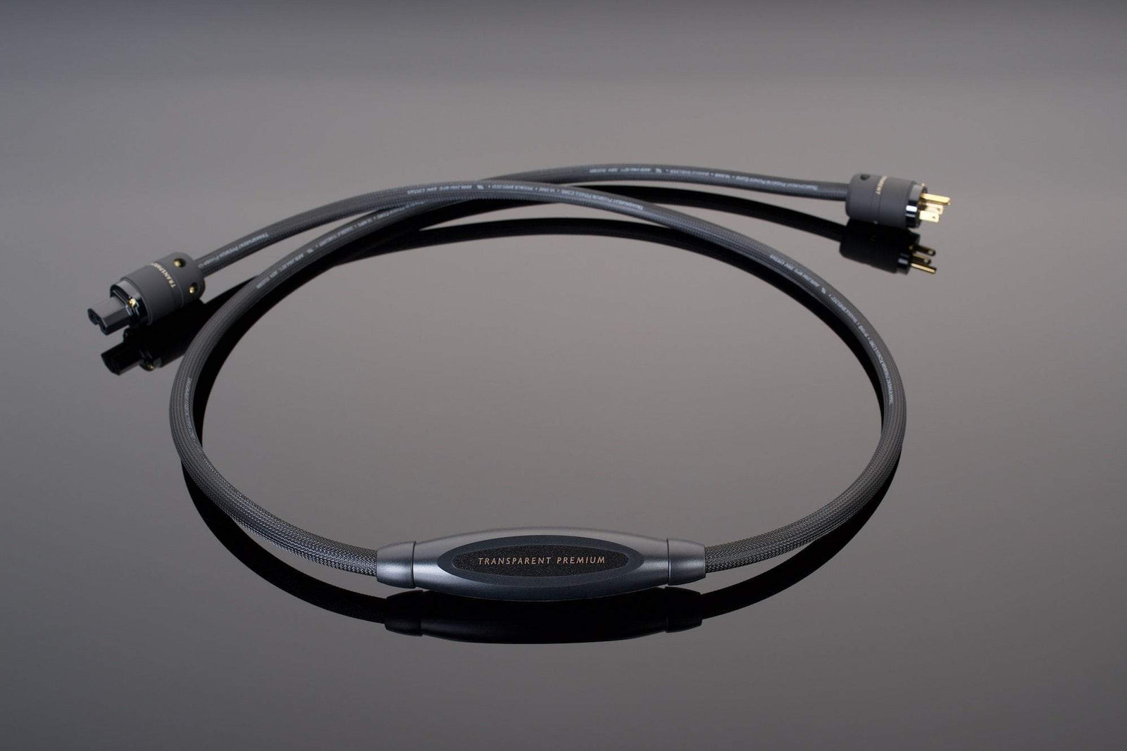 A black, coiled Premium Power Cord from Transparent Audio, labeled "Premium Power Cord" in the center, featuring a standard plug and a three-prong connector on a reflective black surface ensures a noise-free power connection.