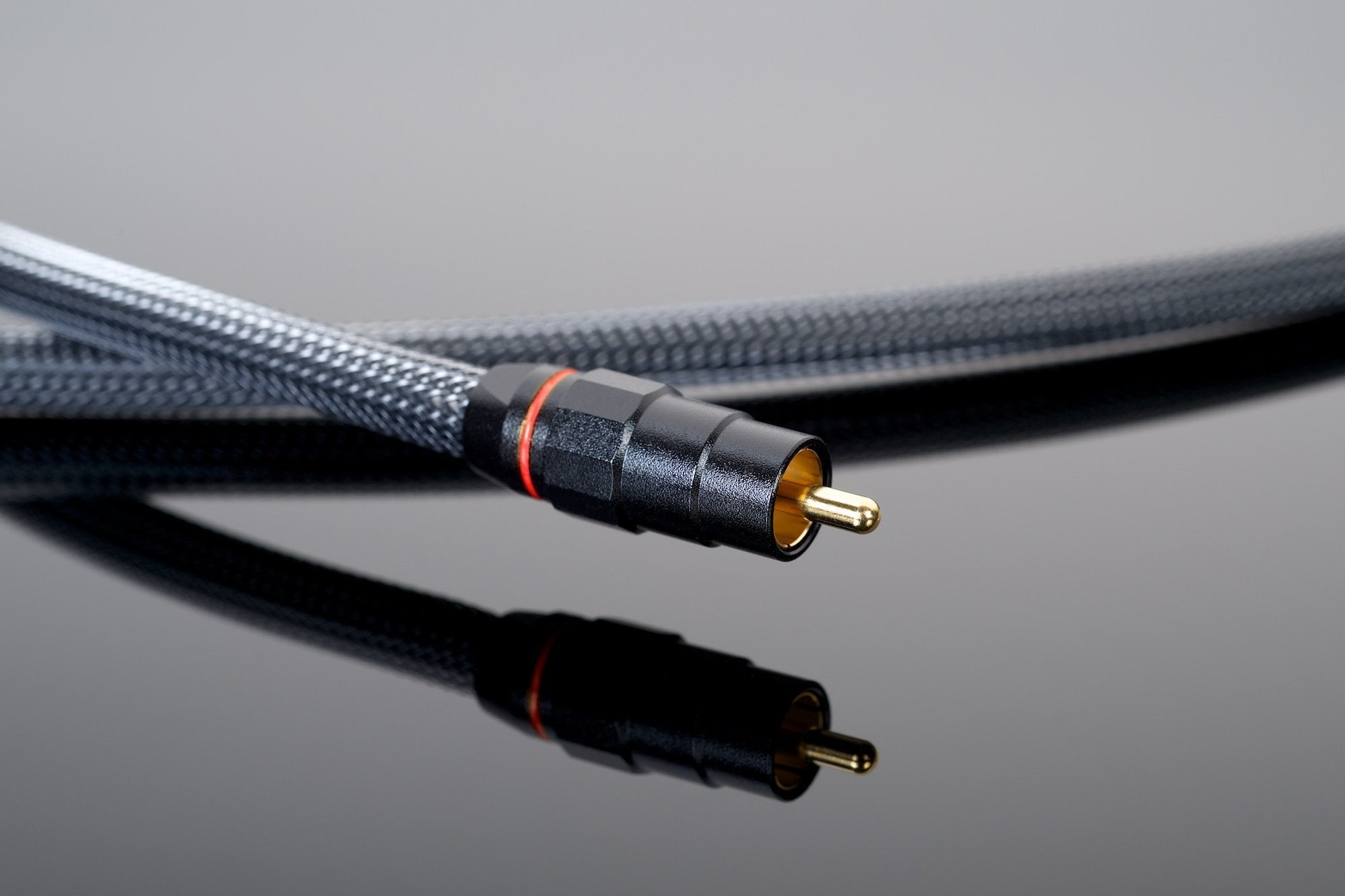 Close-up of a black RCA cable with a gold-plated connector from the Premium 75-Ohm Digital Link by Transparent Audio resting on a reflective black surface.