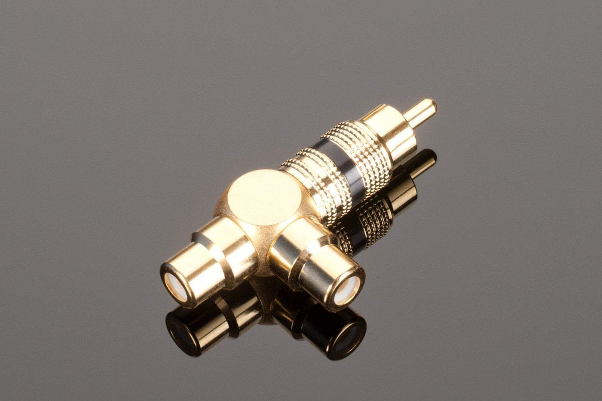 The Transparent Audio RCA Y splitter, featuring two female jacks on one side and a male jack on the other, enhances subwoofer performance with its gold connectors. This gold-plated adapter rests elegantly on a reflective black surface, ensuring both style and superior functionality.