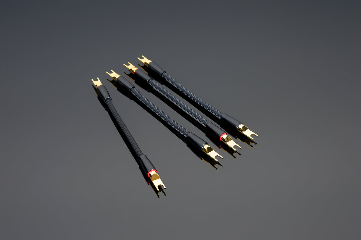 Năm bộ chuyển đổi Transparent Audio Reference hoặc XL Biwire, màu đen và vàng với đầu nối chẻ đôi và sợi đồng có độ tinh khiết cao, được sắp xếp theo đường chéo trên nền xám đậm.