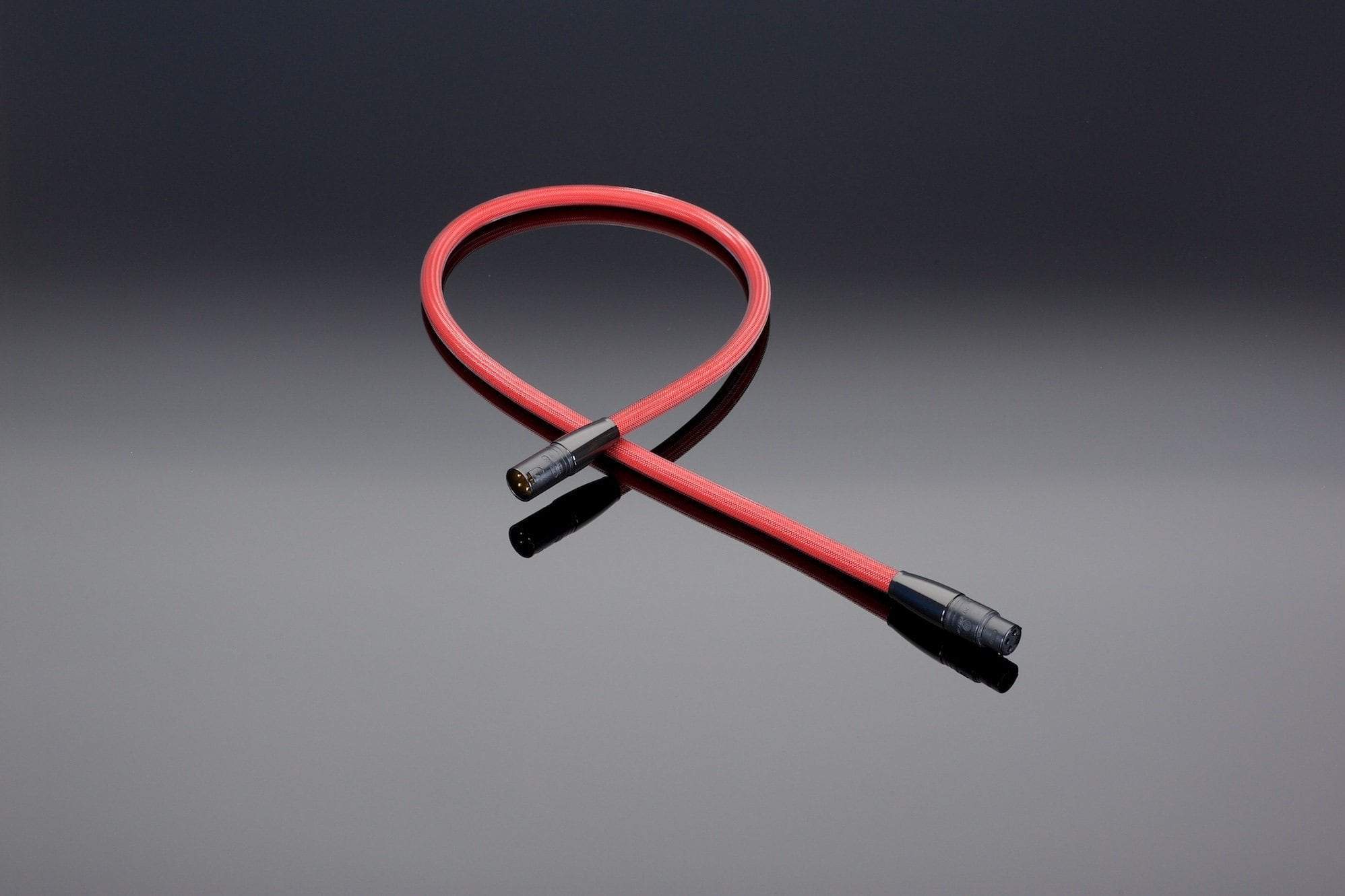 A red cable with two black connectors, coiled into a loose loop, placed against a dark gradient background. This Transparent Audio REFERENCE 110-Ohm AES/EBU Digital Link provides balanced digital connections, significantly reducing noise and jitter for superior audio performance.