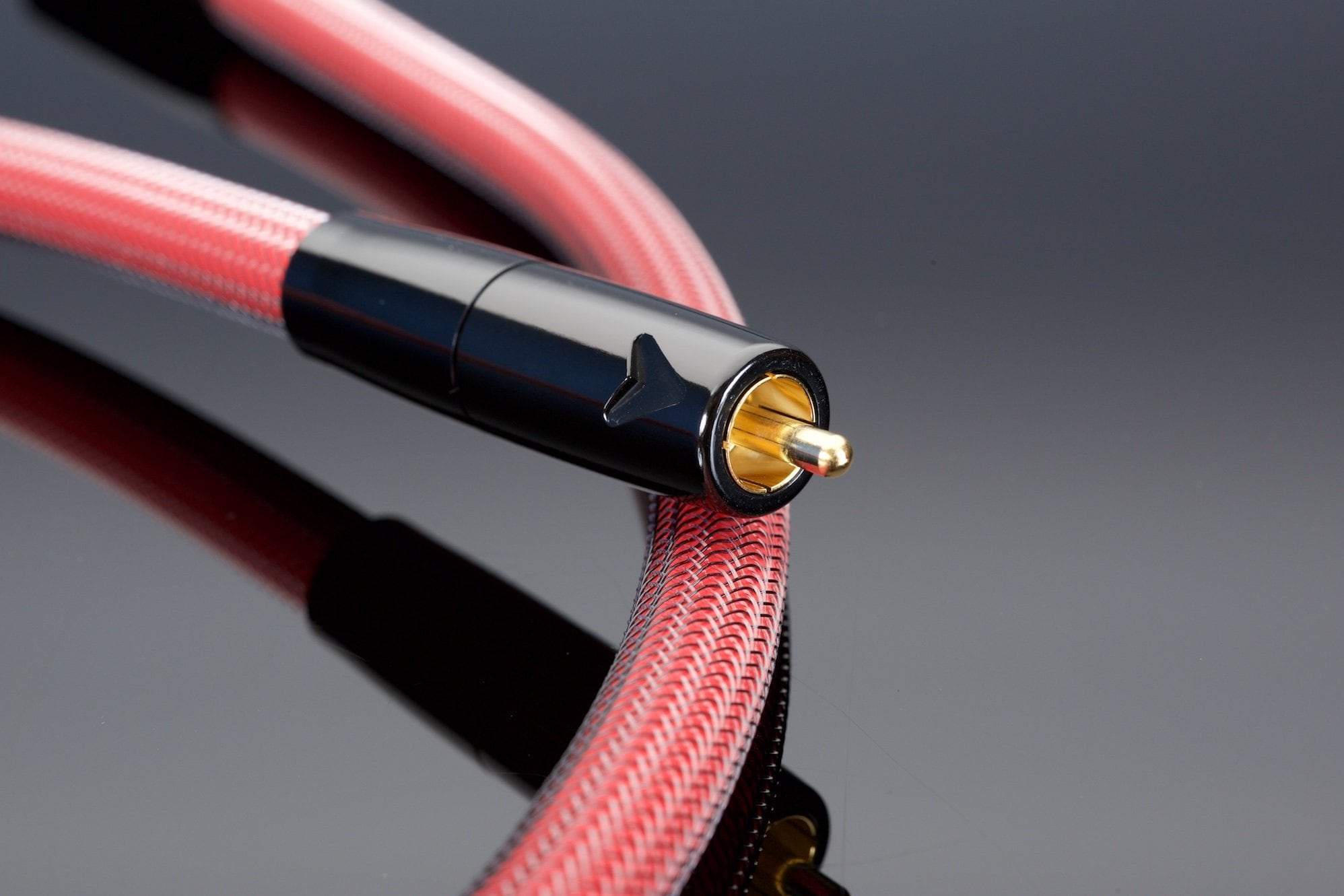 Close-up of an RCA audio cable with a red braided sheath and a black and gold connector, handcrafted in the USA by Transparent Audio, resting on a reflective black surface. This REFERENCE 75-Ohm Digital Link ensures superior 75-ohm impedance stability.