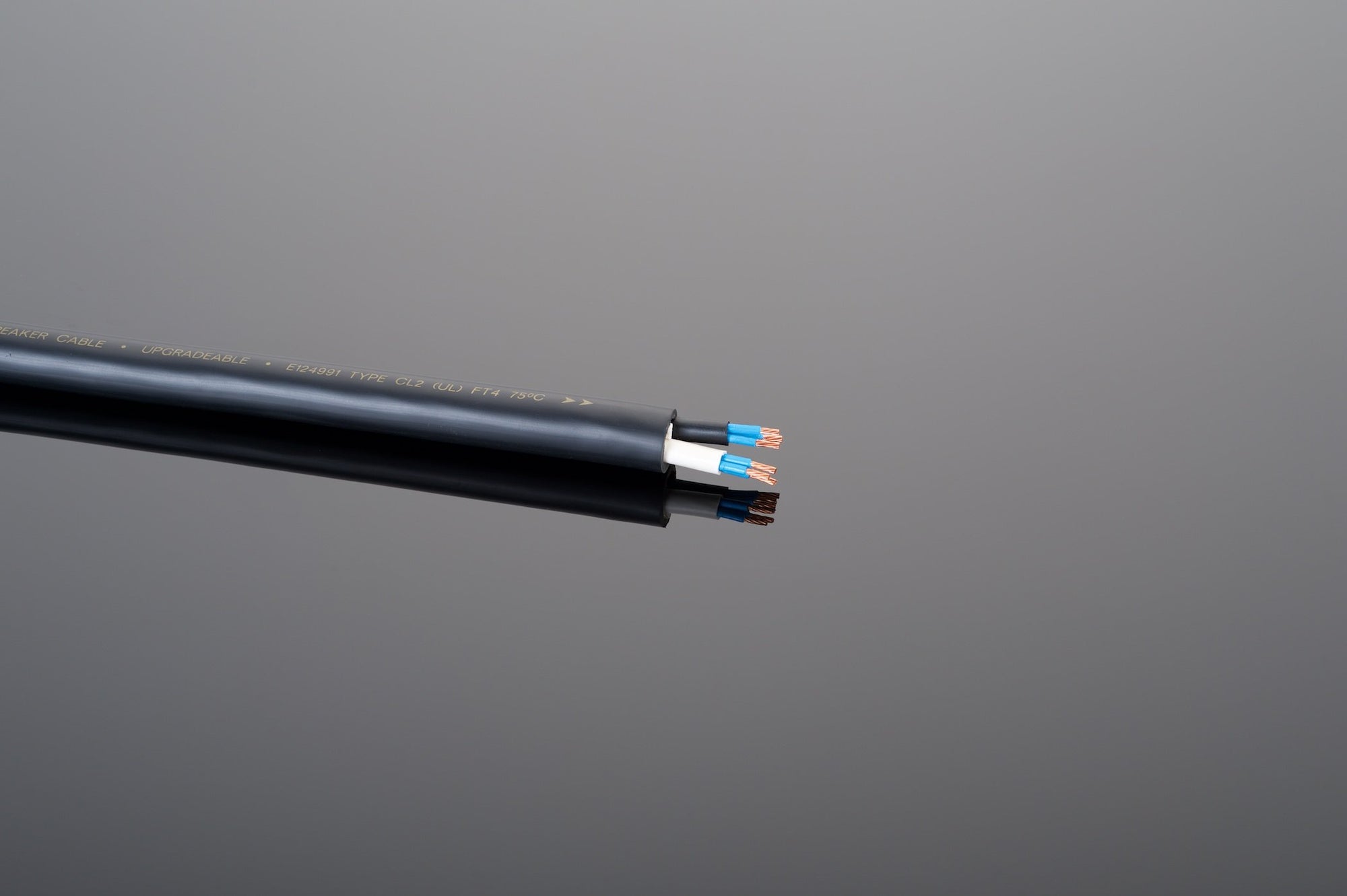 Close-up of The Wall Reference inwall speaker cable by Transparent Audio, featuring three exposed colored wires (blue, brown, and green/yellow) against a gray background—ideal for ultimate music and home entertainment systems.