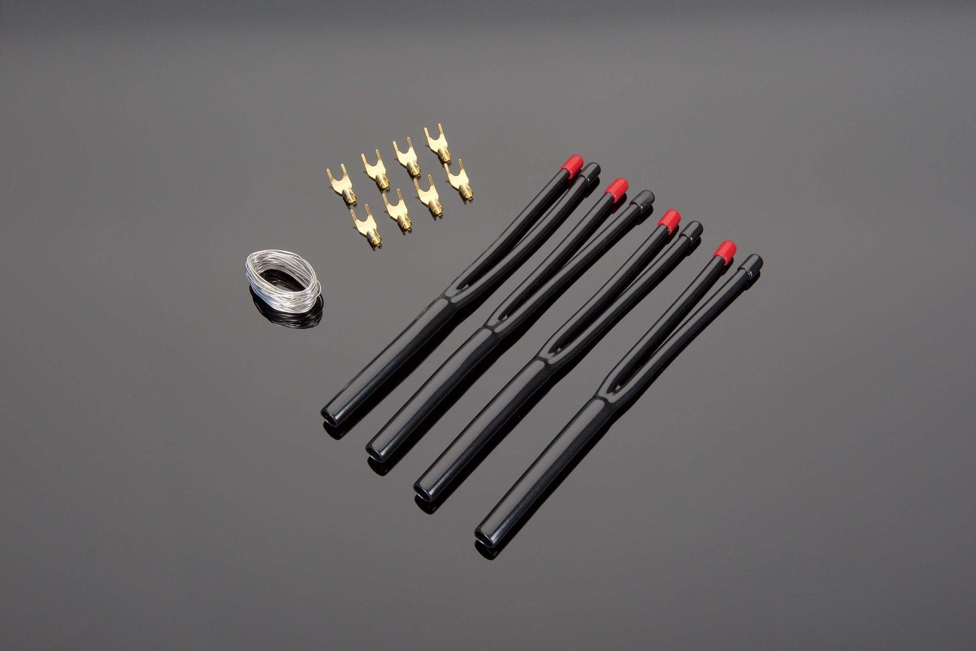 Five black ignition coil packs, six high quality connectors, and a coil of Transparent Audio Solder Termination Kits for High Performance 10-2 DIY Speaker Cable arranged on a black surface.
