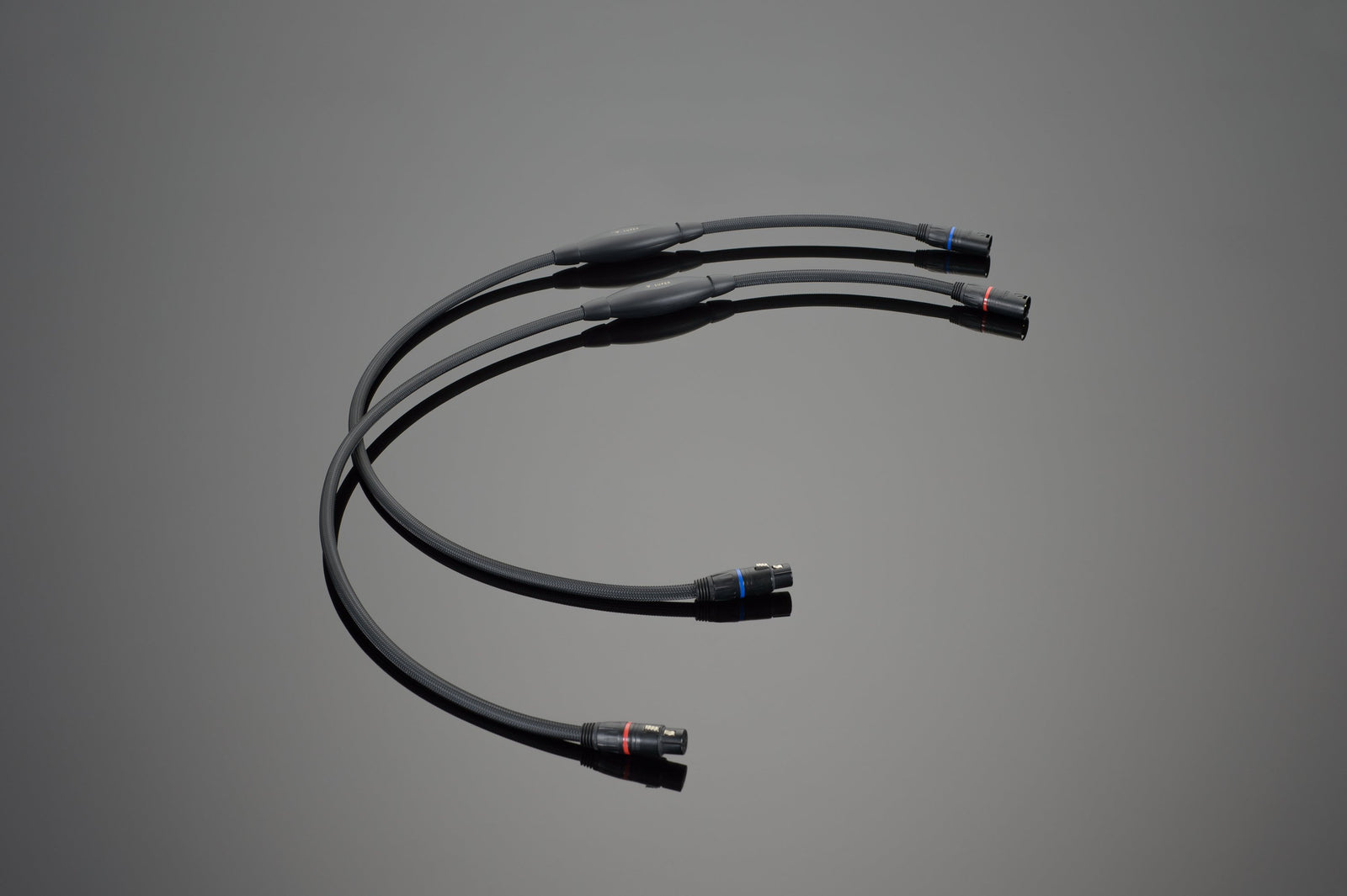 Three black cables with high-quality XLR connectors on each end are laid out in a curved arrangement on a plain gray background. These Transparent Audio SUPER Balanced Interconnects seamlessly blend both form and function.
