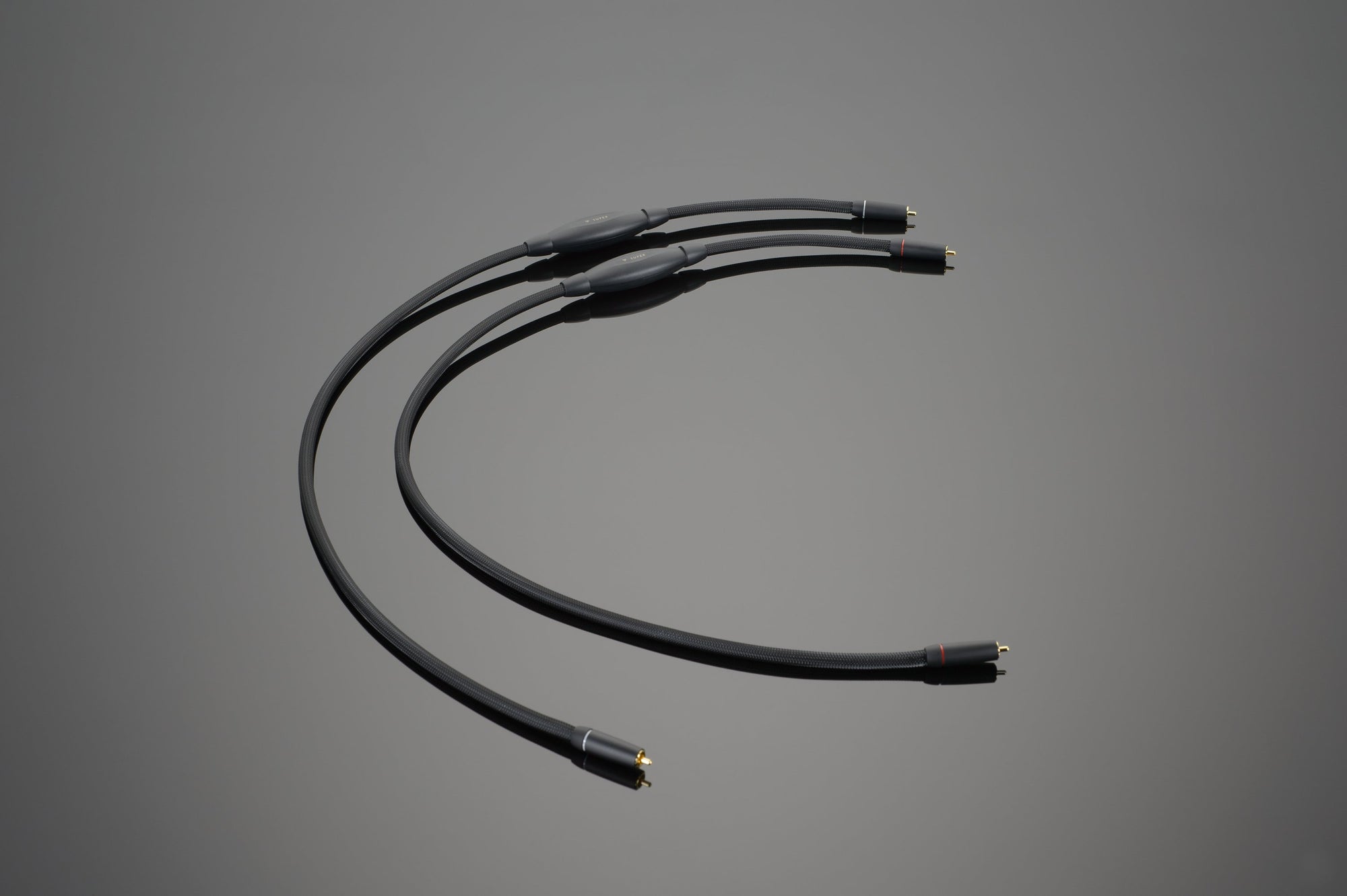 Three SUPER RCA Interconnect cables from Transparent Audio, featuring black exteriors and gold-plated connectors, proudly handcrafted in the USA, arranged in a curved pattern on a plain grey background.