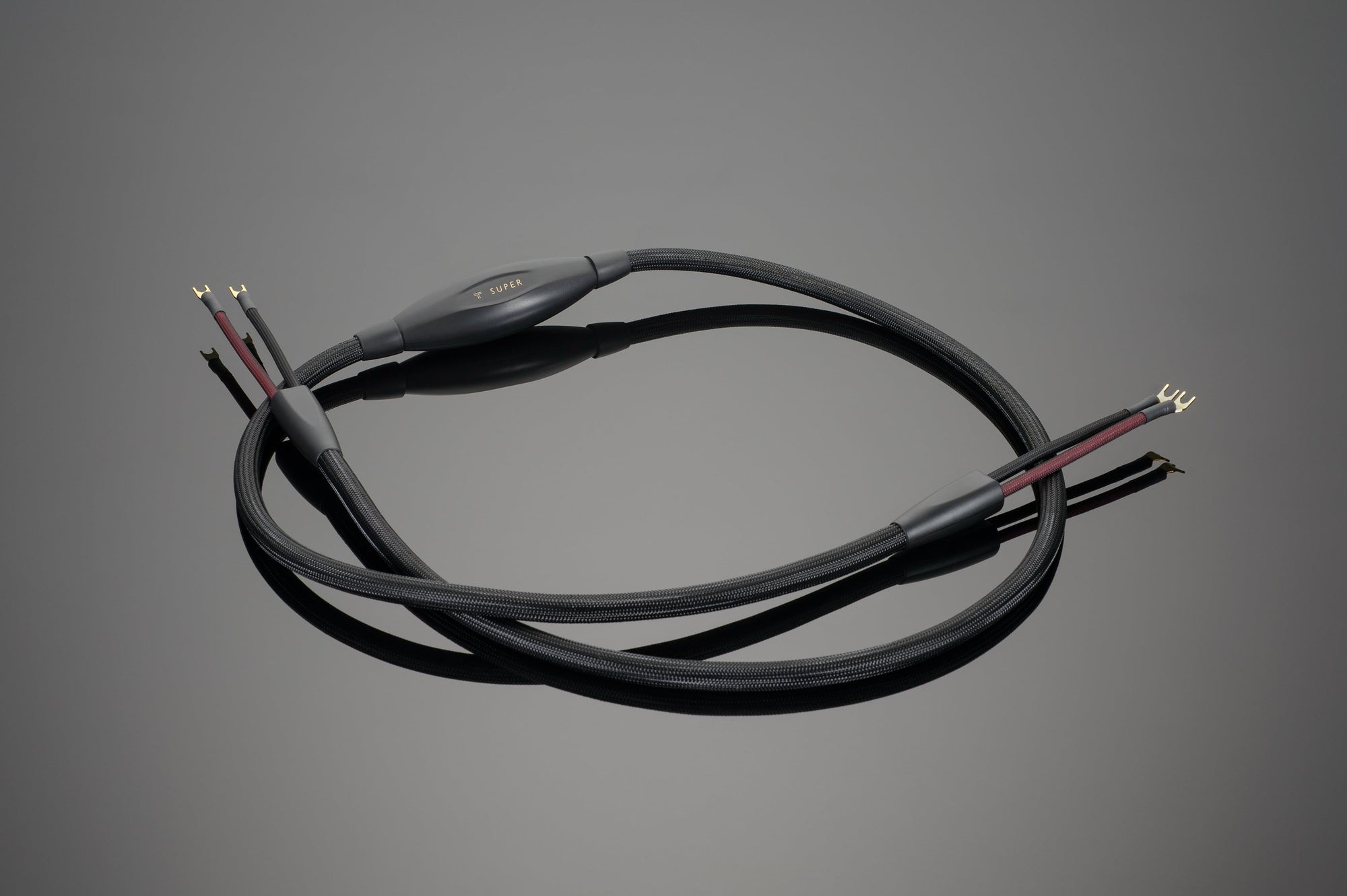 A pair of Transparent Audio's SUPER Speaker Cables in black, featuring gold-plated connectors at both ends, placed on a flat surface—ideal for enhancing your premium music system.