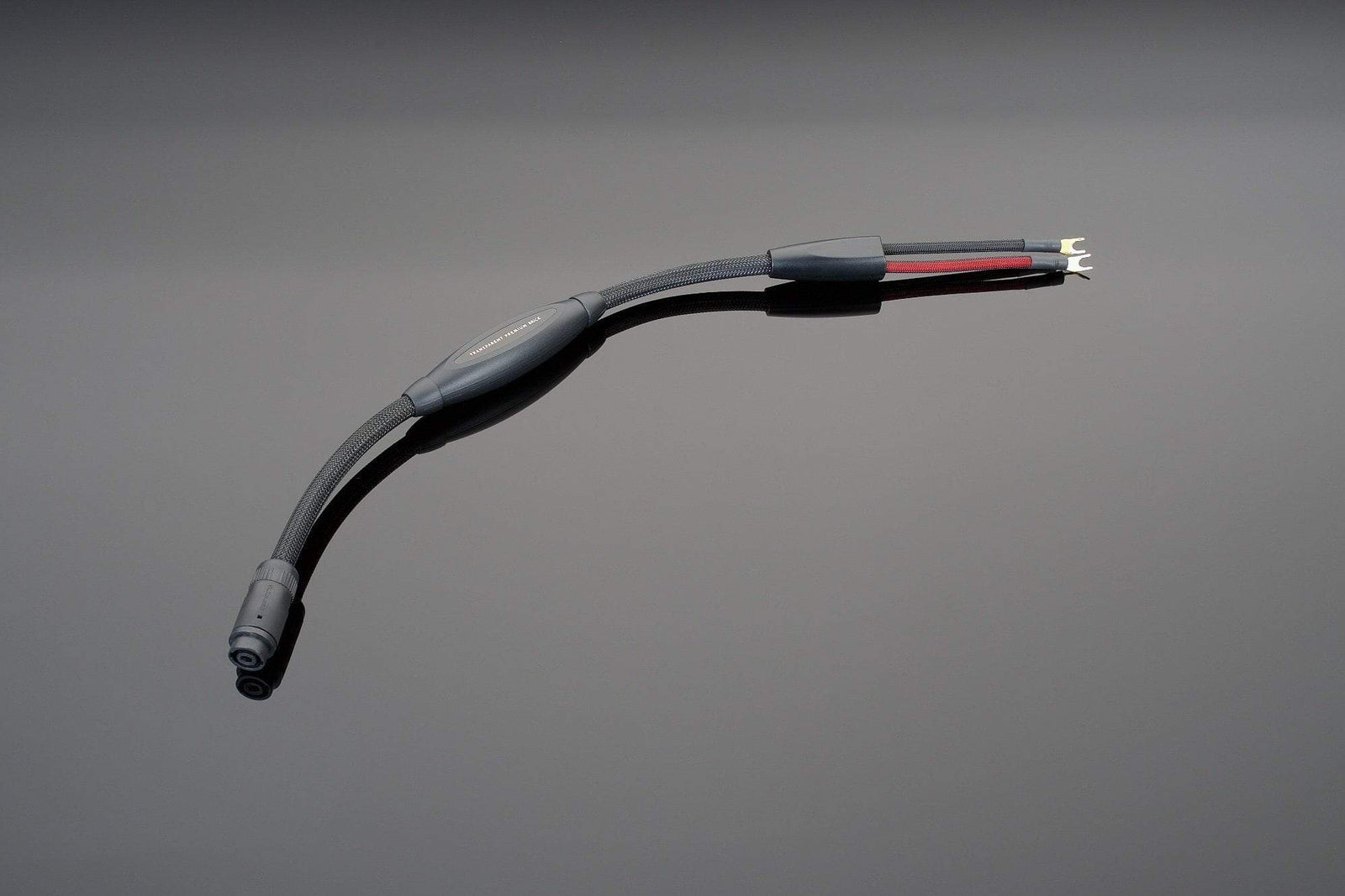 A high-end audio component, The Brick Premium black cable by Transparent Audio, with connectors on each end is positioned on a reflective gray surface.