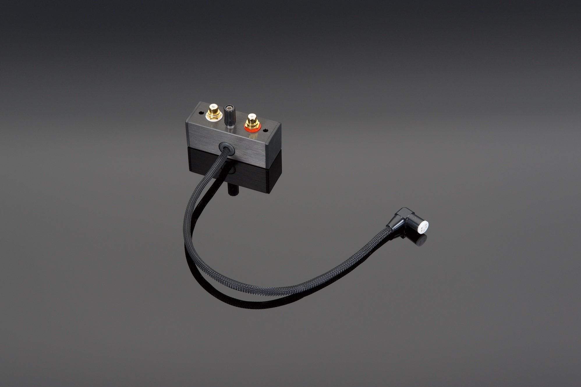 A Transparent Audio Transparent DIN to RCA Adapter featuring a sleek black design with two metal connectors and a flexible tonearm cable, resting on a reflective black surface.