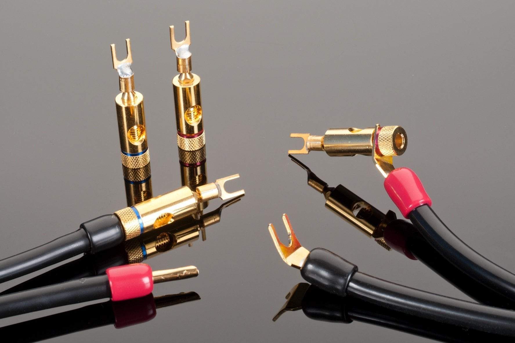 Close-up of Transparent Audio's Transparent Spade to Mini Bar Spade Adapters with gold-plated connectors, displayed on a reflective black surface, evoking the feel of vintage audio components.