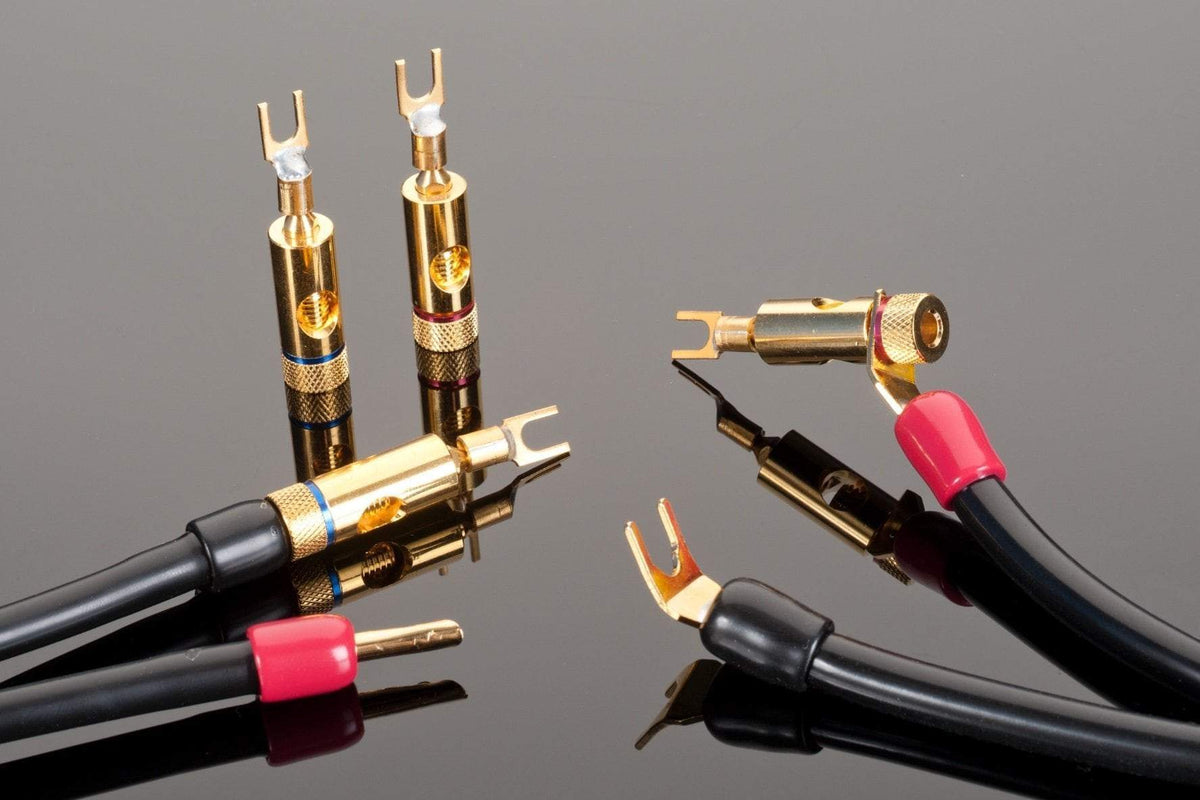 Close-up of Transparent Audio&#39;s Transparent Spade to Mini Bar Spade Adapters with gold-plated connectors, displayed on a reflective black surface, evoking the feel of vintage audio components.