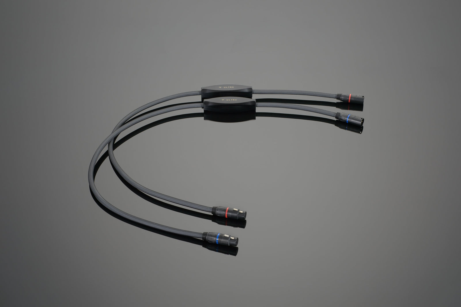 Image of the ULTRA Balanced Interconnect by Transparent Audio, featuring one input and four outputs, each ending in high-quality XLR connectors with color-coded rings. The splitter is placed on a reflective surface.
