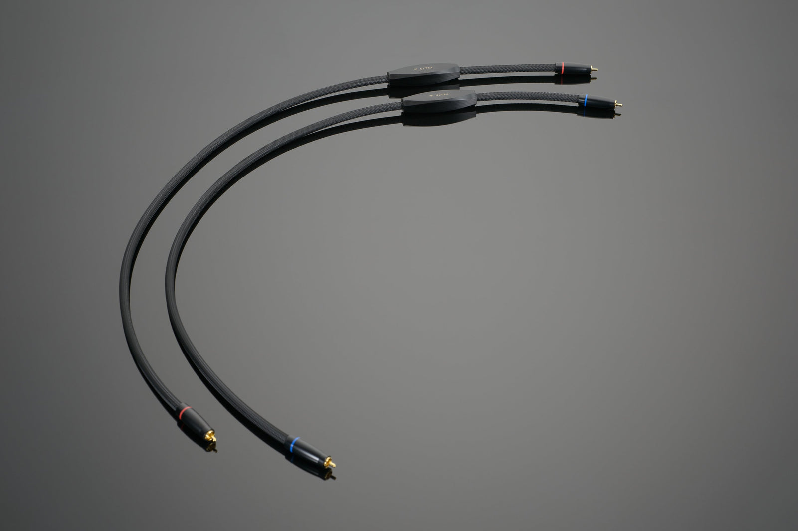 An image depicting two ULTRA RCA Interconnects from Transparent Audio, featuring gold-plated connectors set against a gray background. Each cable showcases a small cylindrical component near the center, with color-coded ends—one red and one blue—providing a LIFELIKE Transparent System.