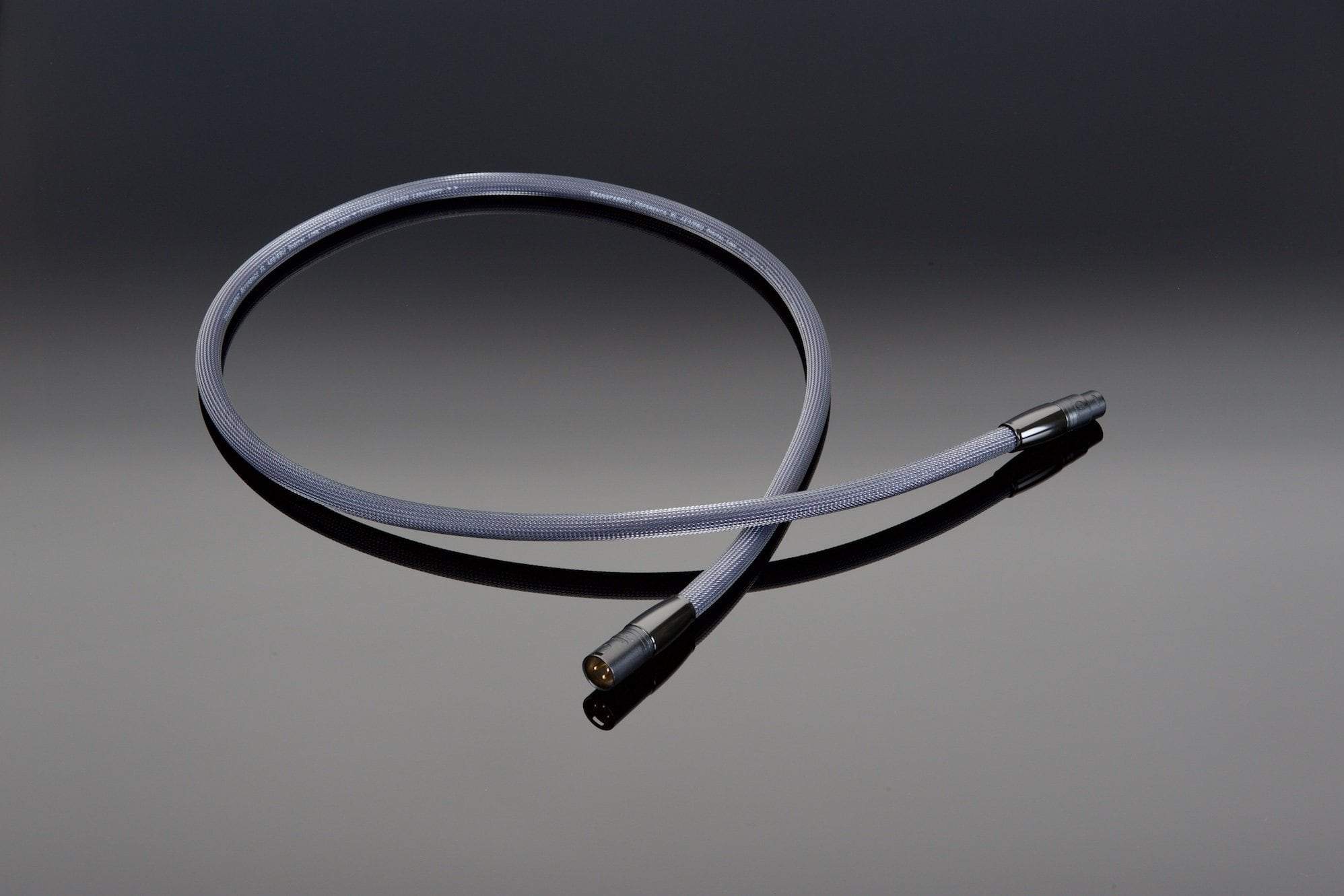 A Transparent Audio XL 110-Ohm AES/EBU Digital Link, a gray, coiled audio cable featuring two metal connectors on each end, lies on a smooth, reflective surface, ensuring 110-ohm impedance stability for balanced digital connections.