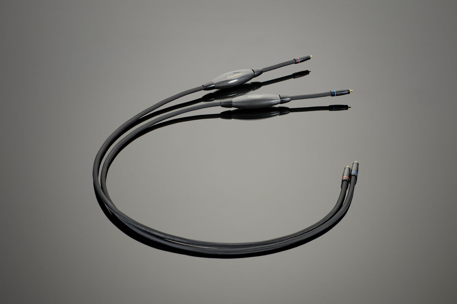 The Transparent Audio XL Phono Interconnect is a black audio cable with three connectors on each end, featuring color-coded tips in red, blue, and black. Ideal for a phonograph set-up, the XL Phono Interconnects are coiled into a loose loop on a flat surface.