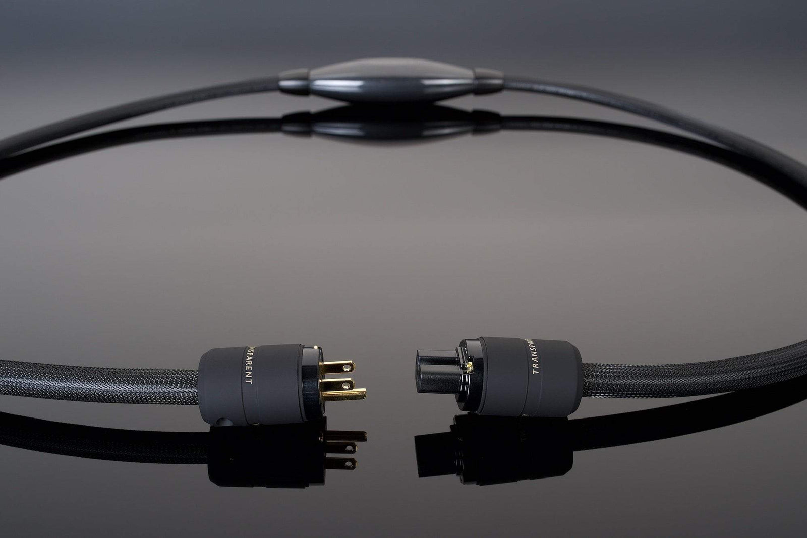 Close-up of the XL Power Cord by Transparent Audio, a black, high-end noise-free power cable with connectors on each end, set against a glossy black surface.