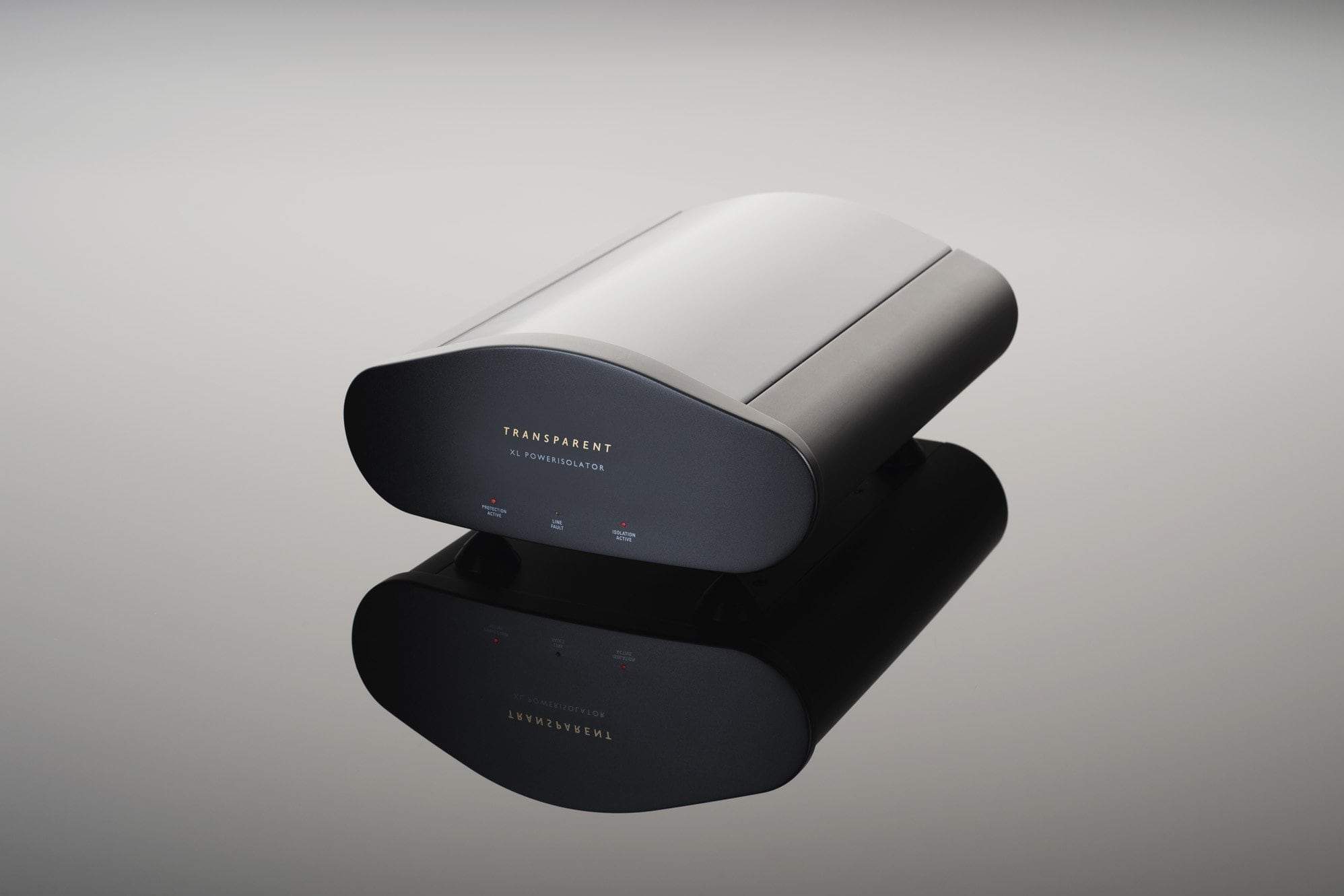 A sleek black electronic device from Transparent Audio, labeled "XL PowerIsolator" with indicator lights, sits on a reflective surface, showcasing its modern design and superior surge-spike protection.
