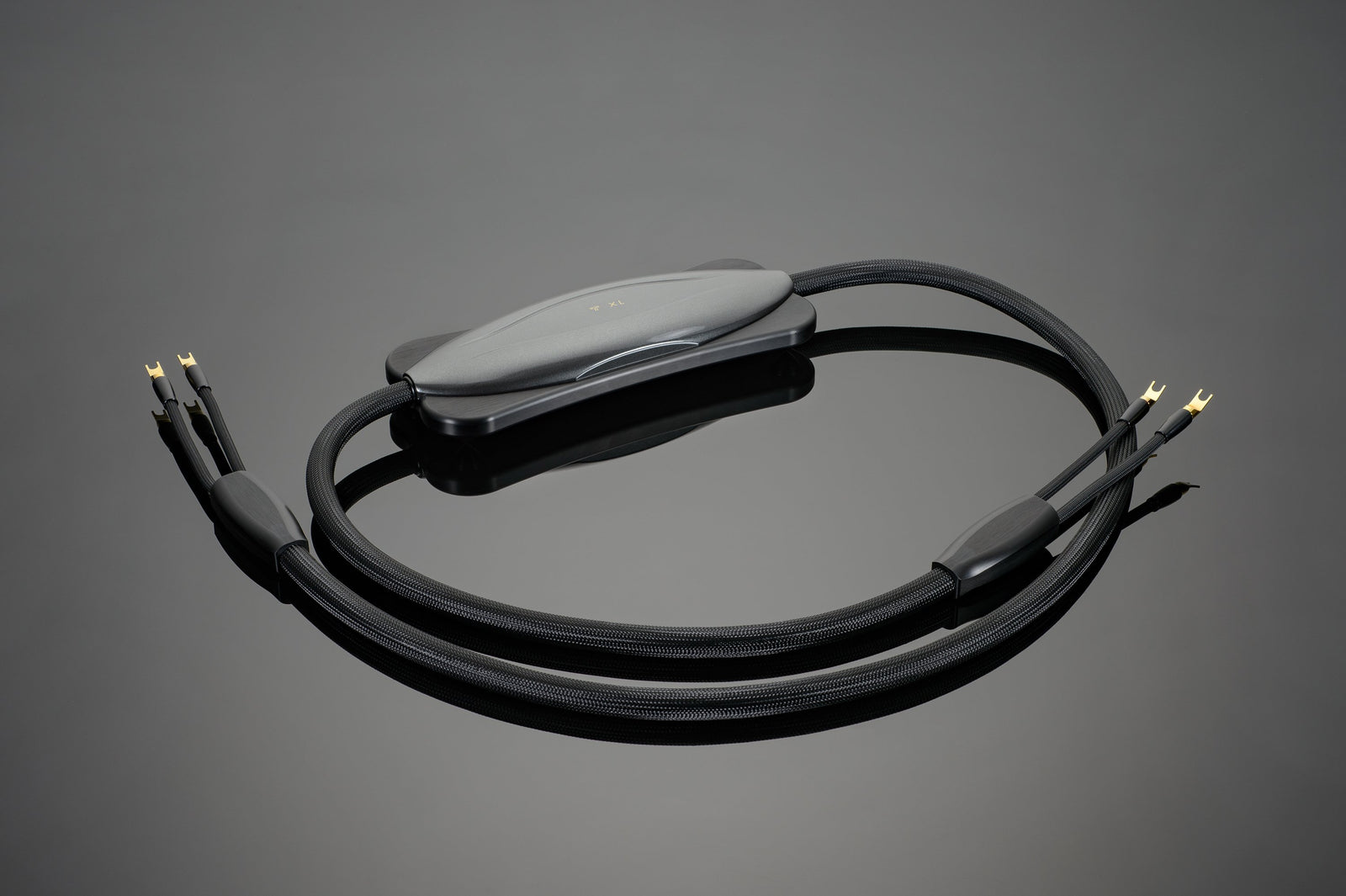 The Transparent Audio XL Speaker Cable, a black, braided marvel featuring gold-plated connectors, displayed against a dark, reflective surface, promises a performance upgrade.